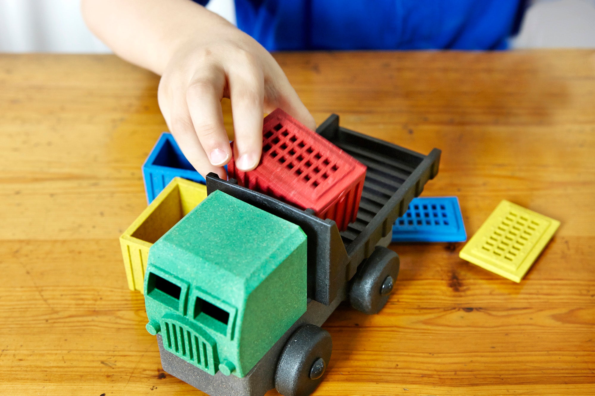 The hand of a small child stacks a red box on the Luke's Toy Factory Toy Cargo Truck